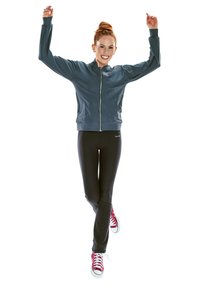 Sportsjakke i mørkegrå med lynlås foran; tætsiddende sorte leggings; røde sneakers med hvide detaljer. Modell er i en dynamisk springpose.