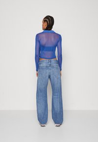 Blue sheer long-sleeve top paired with loose, light-wash denim jeans. Top features a collar; jeans have back pockets and a relaxed fit.