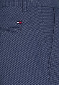 Pantalones a cuadros azul marino con tejido texturizado, que presentan un pequeño logo bordado en rojo, blanco y negro en el bolsillo trasero.