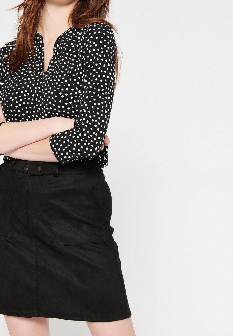 Bluzka w czarno-białe groszki z rękawami do połowy przedramienia, zestawiona z czarną zamszową spódnicą z dwoma przednimi kieszeniami i dopasowaną talią.