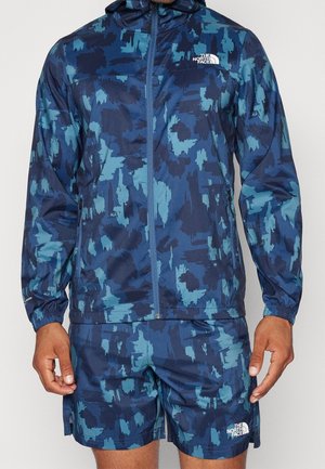 Blue camouflage print jacket and shorts set made of lightweight fabric. Features a hood, full zip, elastic cuffs, and logo accents.