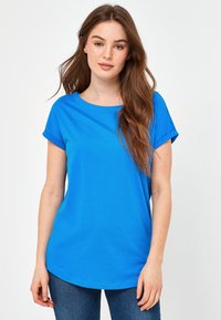 Blå kortærmet T-shirt med rund halsudskæring og opkrøllede ærmer, lavet af blødt stof, parret med mørkeblå jeans.