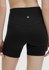 Schwarze, hochgeschnittene Shorts aus dehnbarem Material, mit einem Rautenmuster und dezentem Logo auf der Rückseite, glatten Nähten und klaren Linien.