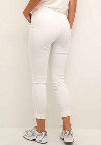 Witte, strakke broek met een elegante uitstraling, voorzien van twee achterzakken en een zachte textuur, gecombineerd met sportieve schoenen met zilveren accenten.