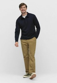 Marinblå långärmad pikétröja med kragdesign, som kombineras med khakibyxor och gröna sneakers med vit sula.