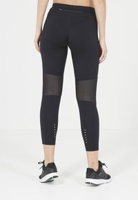 Svarta leggings med nätpaneler, ankellängd, med en ficka med dragkedja och nitar på nederbenet. Mjukt, stretchy material.