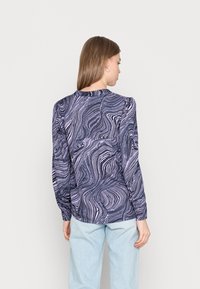 Blusa de mangas longas em púrpura escuro com padrão abstrato branco em espiral. Apresenta mangas volumosas e um decote arredondado.