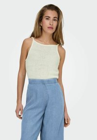 Top de punto acanalado verde claro con tirantes finos, combinado con jeans de pierna ancha en azul claro de cintura alta. Textura suave, diseño sencillo.