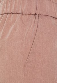 Tecido rosa claro com uma textura suave, apresentando um cós franzido e um bolso lateral. O tecido tem um brilho sutil.