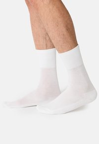 Weiße Baumwollcrew-Socken mit gerippten Bündchen, glatter Textur sowie verstärkten Zehen und Fersen. Entworfen für Komfort und Langlebigkeit.
