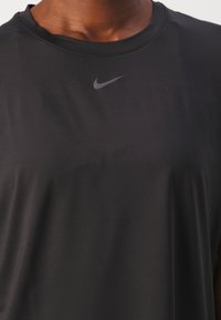 Czarna sportowa koszulka z krótkimi rękawami, o gładkiej fakturze, z odblaskowym szarym logo Nike na klatce piersiowej. Prosty krój z okrągłym dekoltem.