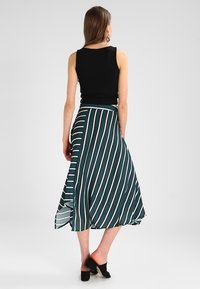 Svart ärmlös topp kombinerad med en lång teal kjol med vita vertikala ränder och en sidoslits; modellen bär svarta klackar.