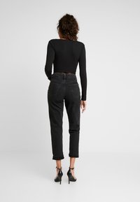 Black long-sleeve top and high-waisted black denim jeans, rolled cuffs, with heels. The outfit features a fitted silhouette and textured fabric.