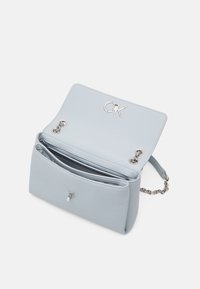 Vaaleansininen nahkainen käsilaukku, jossa on teksturoitu pinta, hopeiset yksityiskohdat ja etuosassa logo. Laukussa on yksi ketjuolkaintaski ja kaksi osastoa.