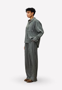 Striped loungewear set in dark green and white, featuring a relaxed-fit shirt with a chest pocket and wide-leg pants. Accented with animal-print slippers.