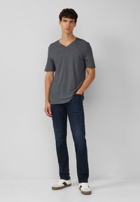 Szary t-shirt z dekoltem w serek i krótkimi rękawami, zestawiony z ciemnoniebieskimi dżinsami i białymi trampkami z czarnymi akcentami. Gładki materiał i luźny krój.