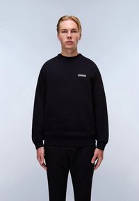 Sudadera negra de mezcla de algodón, con cuello redondo y puños acanalados, y un pequeño logo en el pecho izquierdo. Modelo con pantalones a juego.