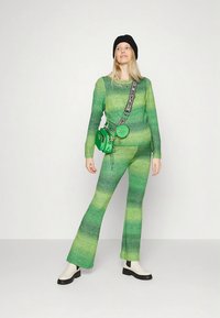 Conjunto de malha verde com duas peças, composto por um top estampado e calças evasê. Acessórios: gorro preto e mala verde de tiracolo. Calçado branco.