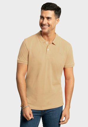 Camisa polo beige con cuello, mangas cortas y tapeta de tres botones. Presenta un pequeño logo en el pecho y una textura suave.