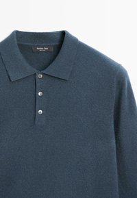 Tmavě modré pletené polo tričko vyrobené z měkké látky, se třemi knoflíky, plochým límečkem a jemnou texturou. Viditelná etiketa.