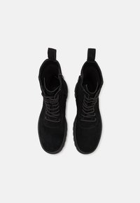 Bottines en suède noir avec une surface texturée, bout arrondi, fermeture à lacets et tirants sur le col pour un enfilage facile.