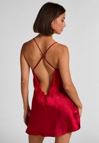 Κόκκινο σατέν νυχτικό με βαθιά V-πλάτη, δαντέλα κατά μήκος του ντεκολτέ, ρυθμιζόμενους λουράκια σε σταυρωτό σχέδιο και λεία, ρέουσα σιλουέτα.