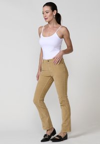 Lichtbruine corduroy broek met een recht model, voorzien van steekzakken, knoopsluiting en gecombineerd met een witte tanktop en zwarte ballerina's.