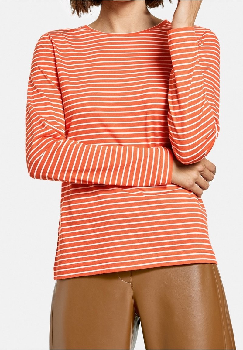 Langärmliges, Rundhalsoberteil in leuchtendem Orange mit weißen horizontalen Streifen, aus weichem Stoff, kombiniert mit braunen Kunstlederhosen.