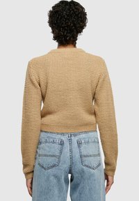 Khaki knitted sweater with a textured pattern, cropped design, and ribbed cuffs. Paired with light blue high-waisted jeans.