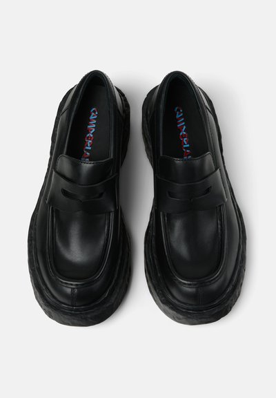 Black leather loafers with a rounded toe, thick sole, and decorative strap. Smooth texture with a contrasting blue and red insole detail.