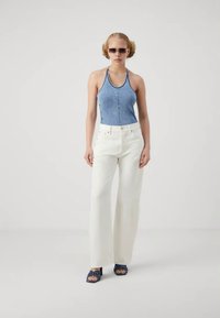 Zila denim halter top kombinēts ar baltām platām biksēm, melnām siksnām augstpapēžu kurpēm un saulesbrillēm; minimālistisks dizains ar tīrām līnijām.