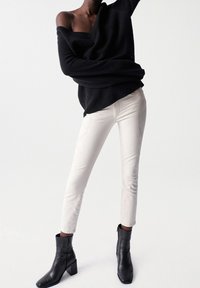 Black oversized knit sweater, white fitted jeans with subtle stitching, and black heeled ankle boots, emphasizing texture and contrast.