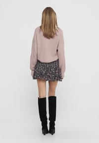 Lichtroze gebreide trui, zwarte bloemen mini-rok met ruffles en aansluitende zwarte kniehoge laarzen met hoge hakken. Achteraanzicht.