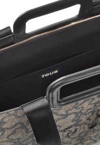 Czarna torba tote z wzorem, z dwiema krótkimi rączkami, z zewnętrzną warstwą z materiału, zamknięciem na zamek błyskawiczny i metką z logo wewnątrz. Wnętrze wyłożone jest czarnym materiałem.