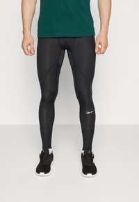Leggings de desempenho pretos com um ajuste justo, textura suave e costuras contrastantes, combinados com sapatilhas de desporto pretas.