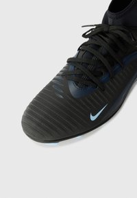 Cizmă de fotbal neagră cu un material texturat, având accente și șireturi de culoare albastră închisă. Are un vârf rotunjit și este concepută pentru aderență.