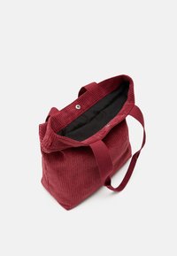 Borsa tote in corduroy rosso con due manici, chiusura a bottone a pressione e foderatura interna in tessuto nero, esposta aperta su sfondo bianco.