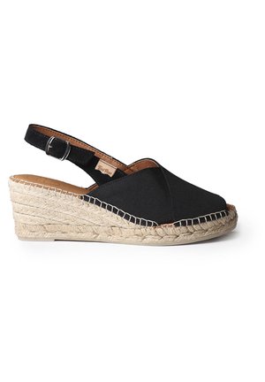 Czarny sandał na klinie z tkaniny, z plecioną podeszwą z juta oraz regulowanym paskiem wokół kostki z srebrną klamrą, widoczny z boku na białym tle.