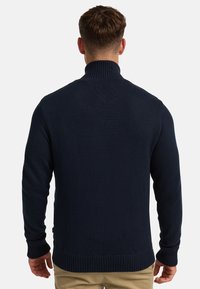 Navy blue knit sweater with a high collar, ribbed cuffs and hem, featuring a textured fabric. Back view shows seamless design.
