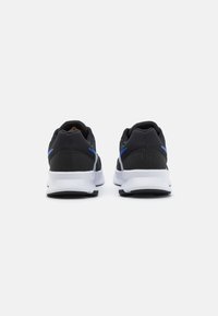 Chaussures de sport noires avec une tige texturée, comportant des accents bleus et une semelle blanche, vues de dos.