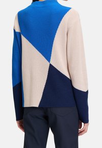 Pull color block avec sections bleu, crème et marine. Fabriqué en maille côtelée avec un col montant et une coupe décontractée.