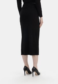 Schwarzer, gerippter Midirock mit tailliertem Design, das eine glatte Textur zeigt, kombiniert mit schwarzen High Heels.