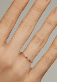 Anillo contorneado en oro rosado con cinco pequeños acentos en forma de estrella que cuentan con piedras transparentes. Banda suave con un acabado pulido.