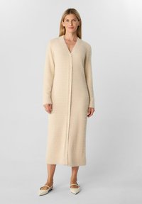 Cardigan lungo beige realizzato in un tessuto morbido e texture, con scollatura a V, chiusura con bottoni discreta e maniche lunghe. Finitura liscia.