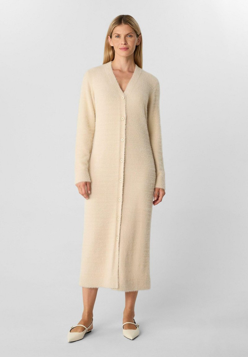 Cardigan lungo beige realizzato in un tessuto morbido e texture, con scollatura a V, chiusura con bottoni discreta e maniche lunghe. Finitura liscia.