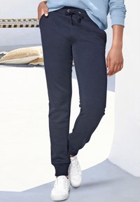Navyblaue Sweatpants mit elastischem Bund und Kordelzug. Eng anliegende Bündchen an den Knöcheln und Seitentaschen. Kombiniert mit weißen Turnschuhen.
