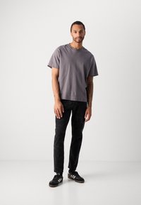 Gray cotton t-shirt with a relaxed fit, short sleeves, and crew neckline paired with black, textured jeans and black athletic shoes.