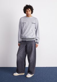 Grå sweatshirt med sort skrift, ribbet halsudskæring og sorte stribede manchetter. Bred grå denim bukser med løs pasform. Hvide sneakers.