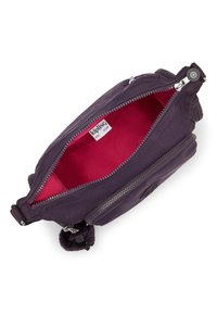 Lilla nylon taske med lynlås, der har en lys pink indvendig foring og en pom-pom accent, som viser en tekstureret overflade og logo.
