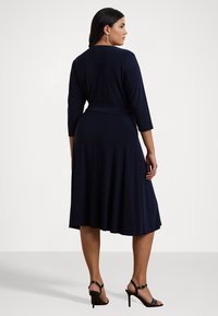 Abito blu navy, lungo fino al ginocchio, realizzato in morbido tessuto, con maniche a tre quarti e vita aderente con gonna svasata; design semplice.